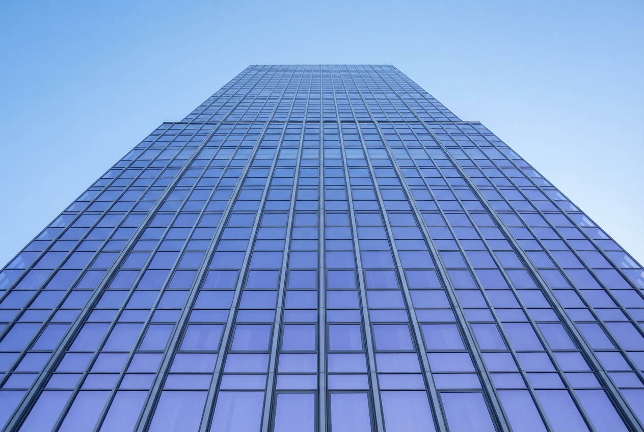 Low-angle view of a blue glass skyscraper with a symmetrical grid façade against a clear sky.